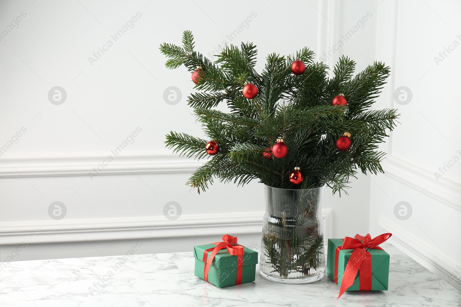 Photo of Beautiful decorated fir tree branches and Christmas gifts on table near white wall