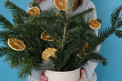 Photo of Woman holding beautiful Christmas composition of fir tree branches decorated with dried orange slices on blue background, closeup