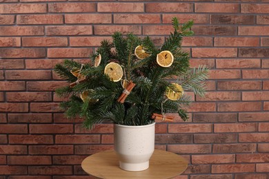 Photo of Beautiful Christmas composition of fir tree branches decorated with dried orange slices and cinnamon sticks on table near brick wall