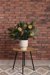 Photo of Beautiful Christmas composition of fir tree branches decorated with dried orange slices and cinnamon sticks on table near brick wall