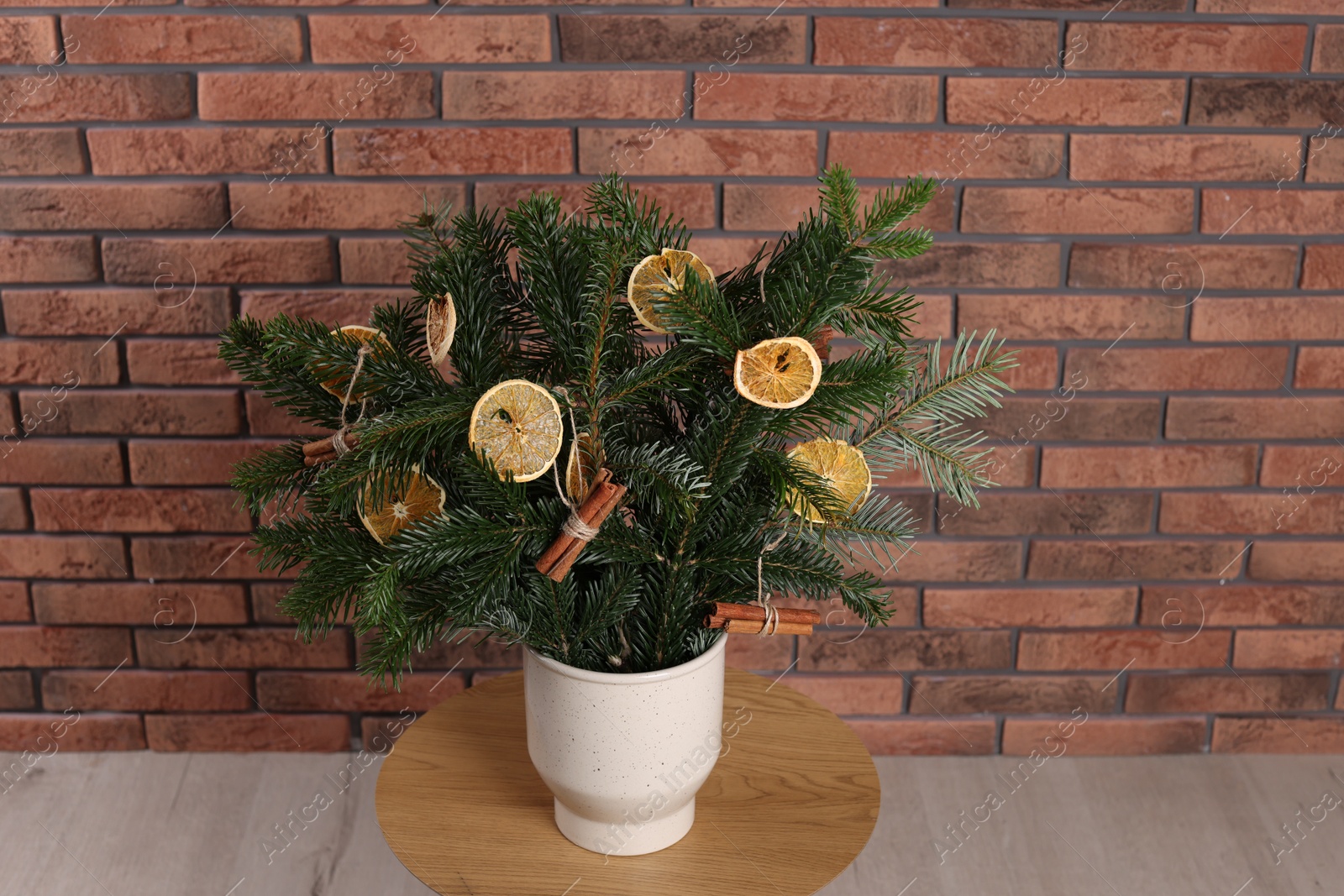 Photo of Beautiful Christmas composition of fir tree branches decorated with dried orange slices and cinnamon sticks on table near brick wall