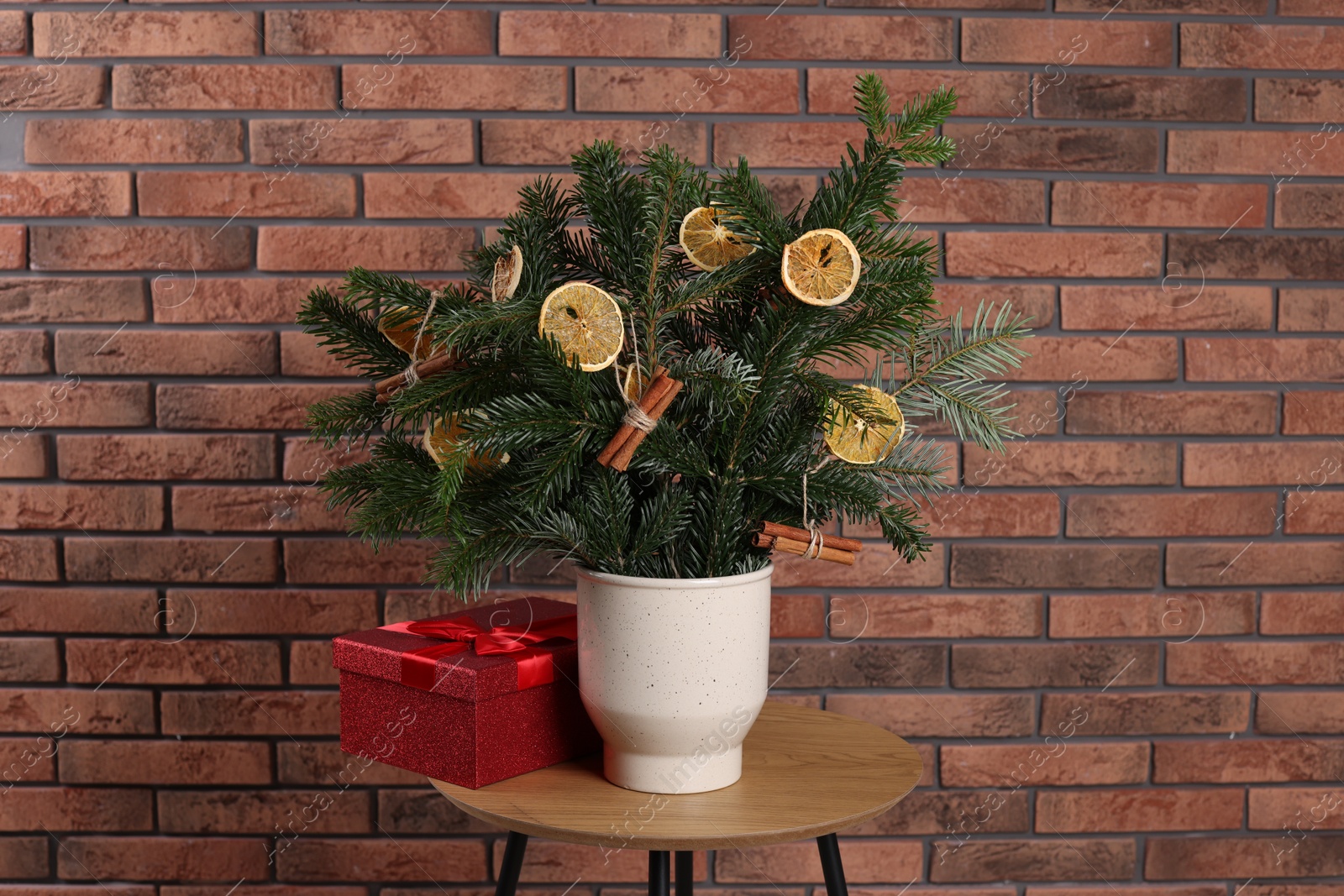 Photo of Beautiful composition of decorated fir tree branches and Christmas gift on table near brick wall