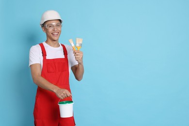 Photo of Portrait of young decorator with bucket and brushes on light blue background, space for text