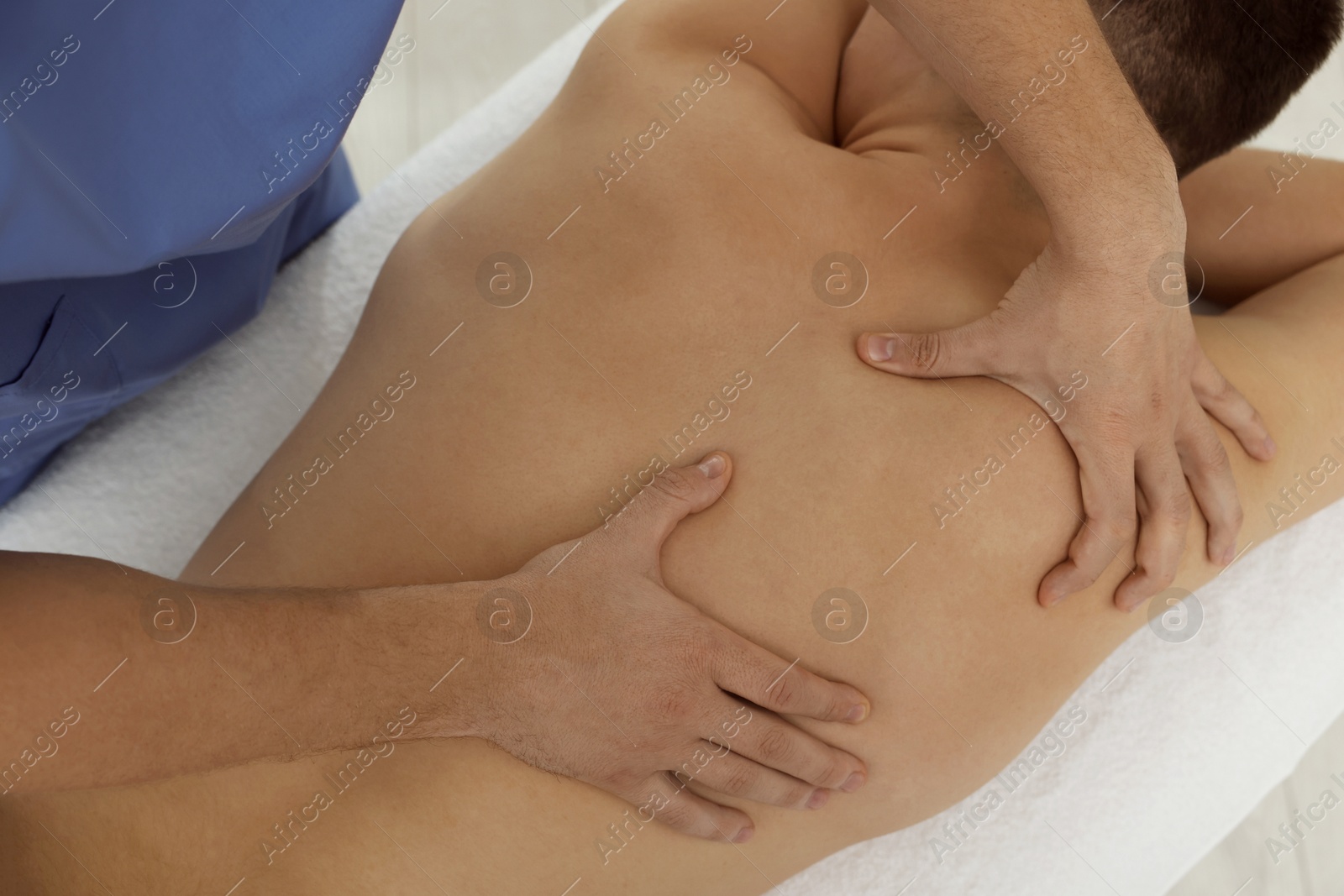 Photo of Osteopath massaging man's back in clinic, above view. Manual therapy