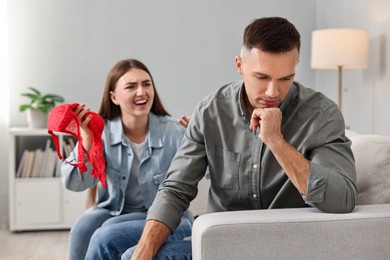 Emotional wife with mistress bra as proof screaming at her unfaithful husband while he ignoring her indoors, selective focus