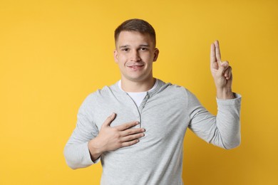 Photo of Man showing oath gesture on orange background. Making promise