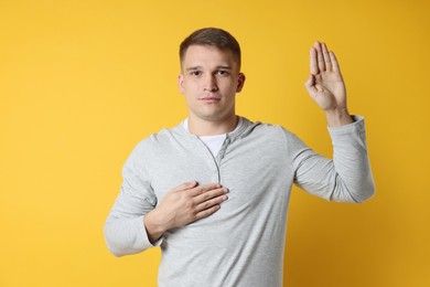 Man making promise with raised hand on orange background. Oath gesture