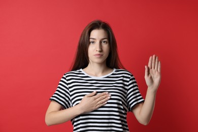 Photo of Woman making promise with raised hand on red background. Oath gesture