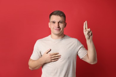 Photo of Man showing oath gesture on red background. Making promise