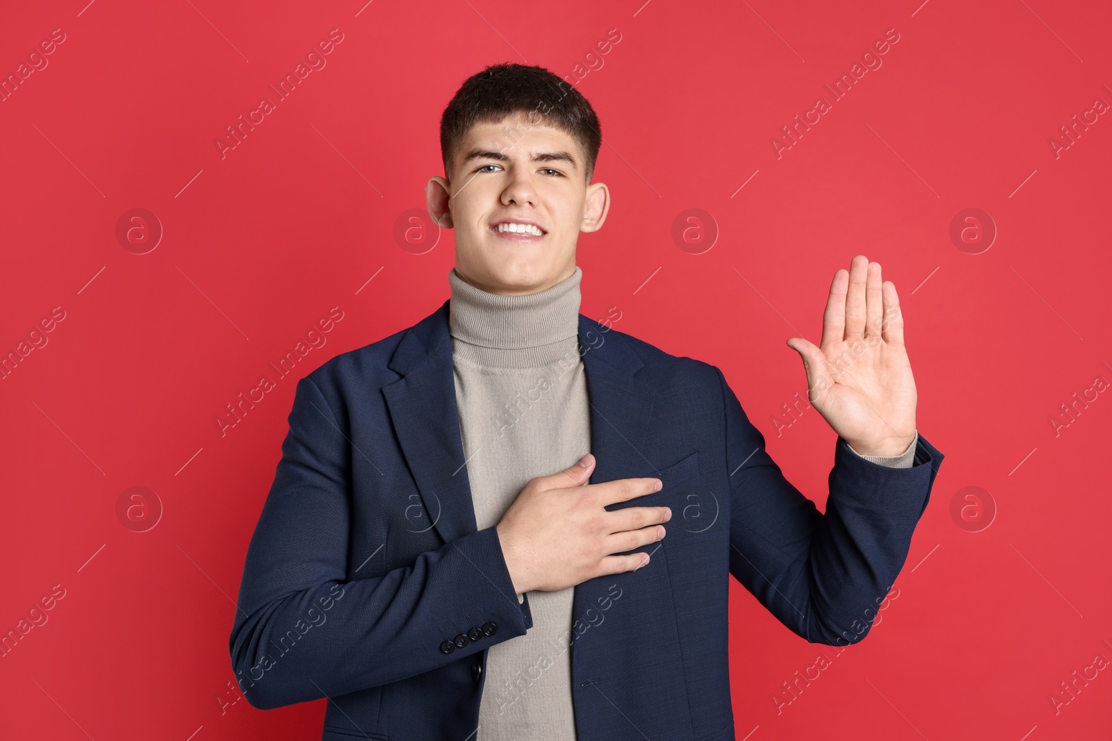 Photo of Man making promise with raised hand on red background. Oath gesture