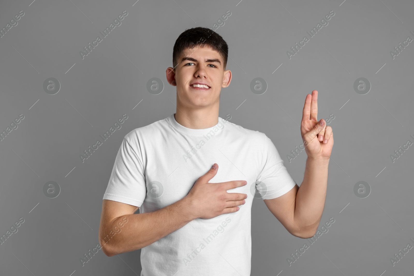 Photo of Man showing oath gesture on grey background. Making promise