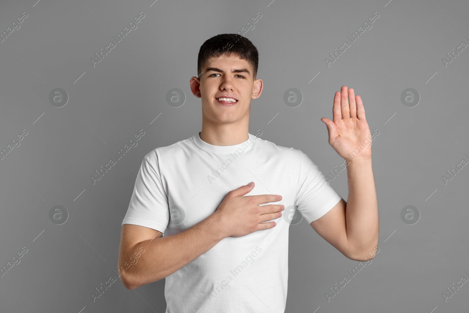 Photo of Man making promise with raised hand on grey background. Oath gesture