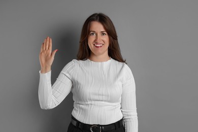 Photo of Woman making promise with raised hand on grey background. Oath gesture