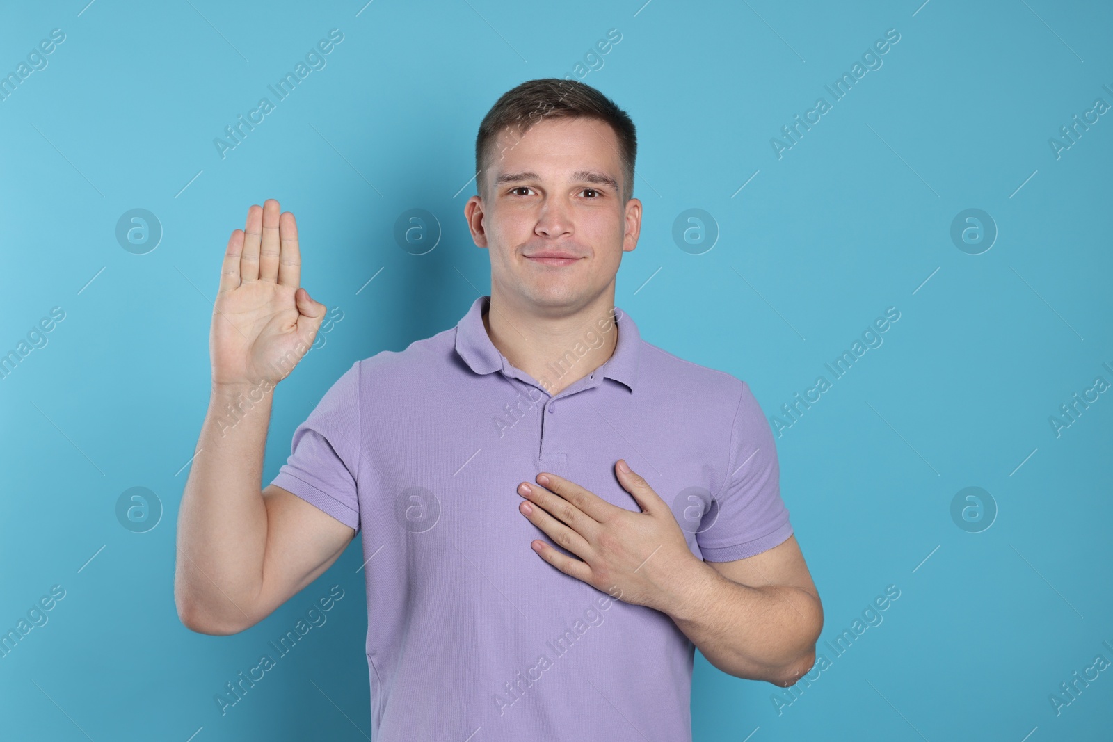 Photo of Man making promise with raised hand on light blue background. Oath gesture