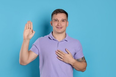 Photo of Man making promise with raised hand on light blue background. Oath gesture