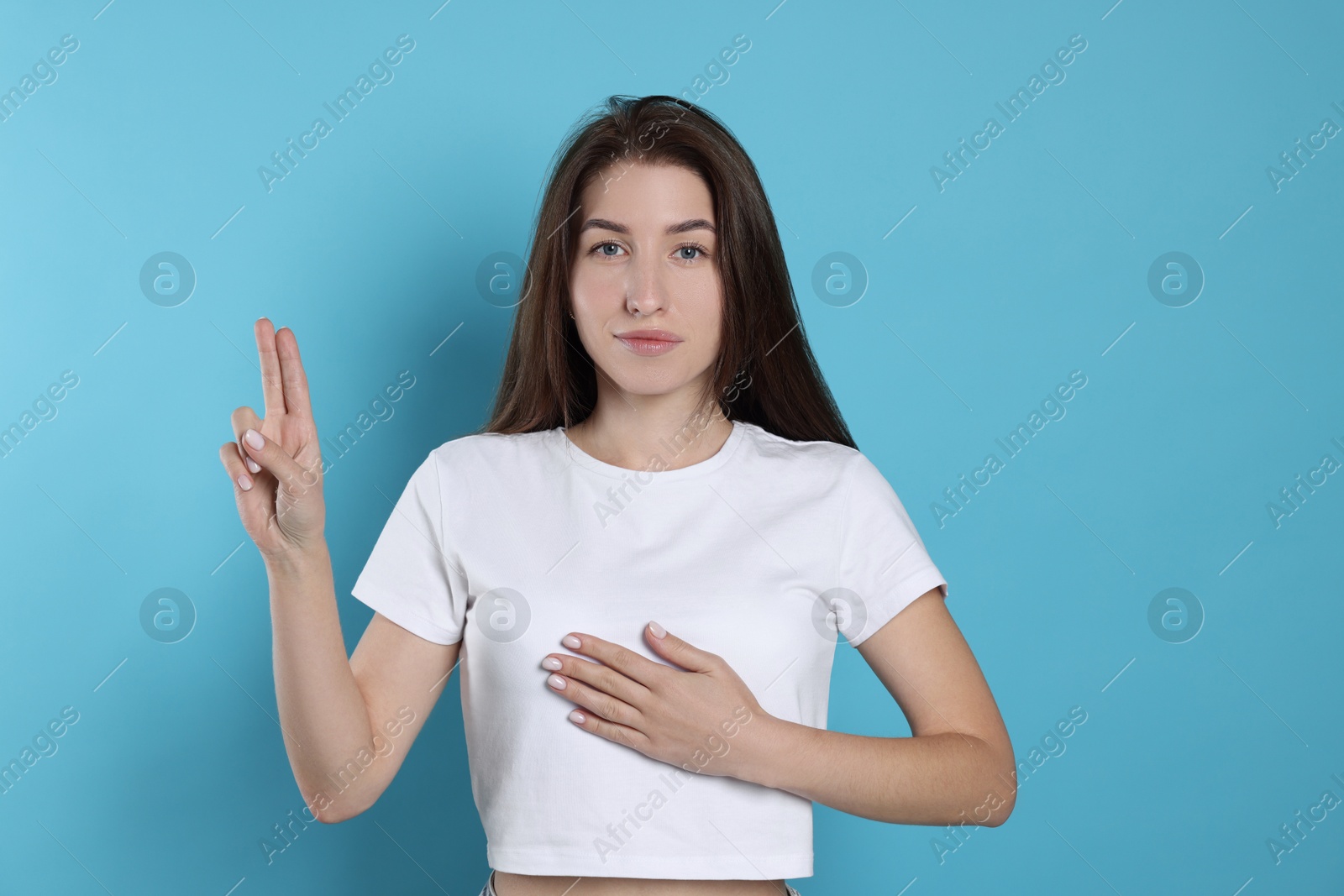 Photo of Woman showing oath gesture on light blue background. Making promise