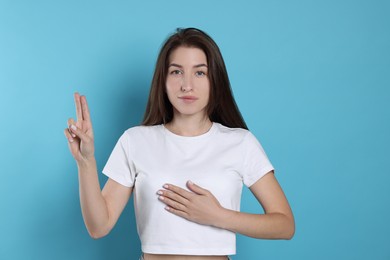 Photo of Woman showing oath gesture on light blue background. Making promise