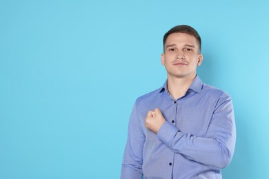 Photo of Man making promise on light blue background, space for text. Oath gesture