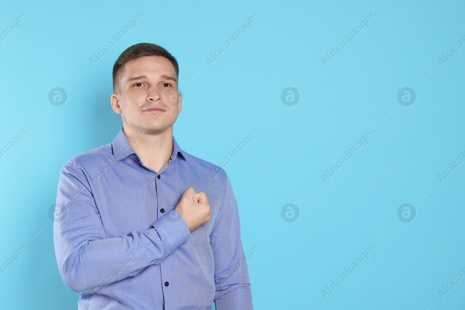 Photo of Man making promise on light blue background, space for text. Oath gesture