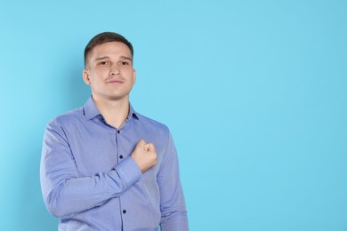 Man making promise on light blue background, space for text. Oath gesture