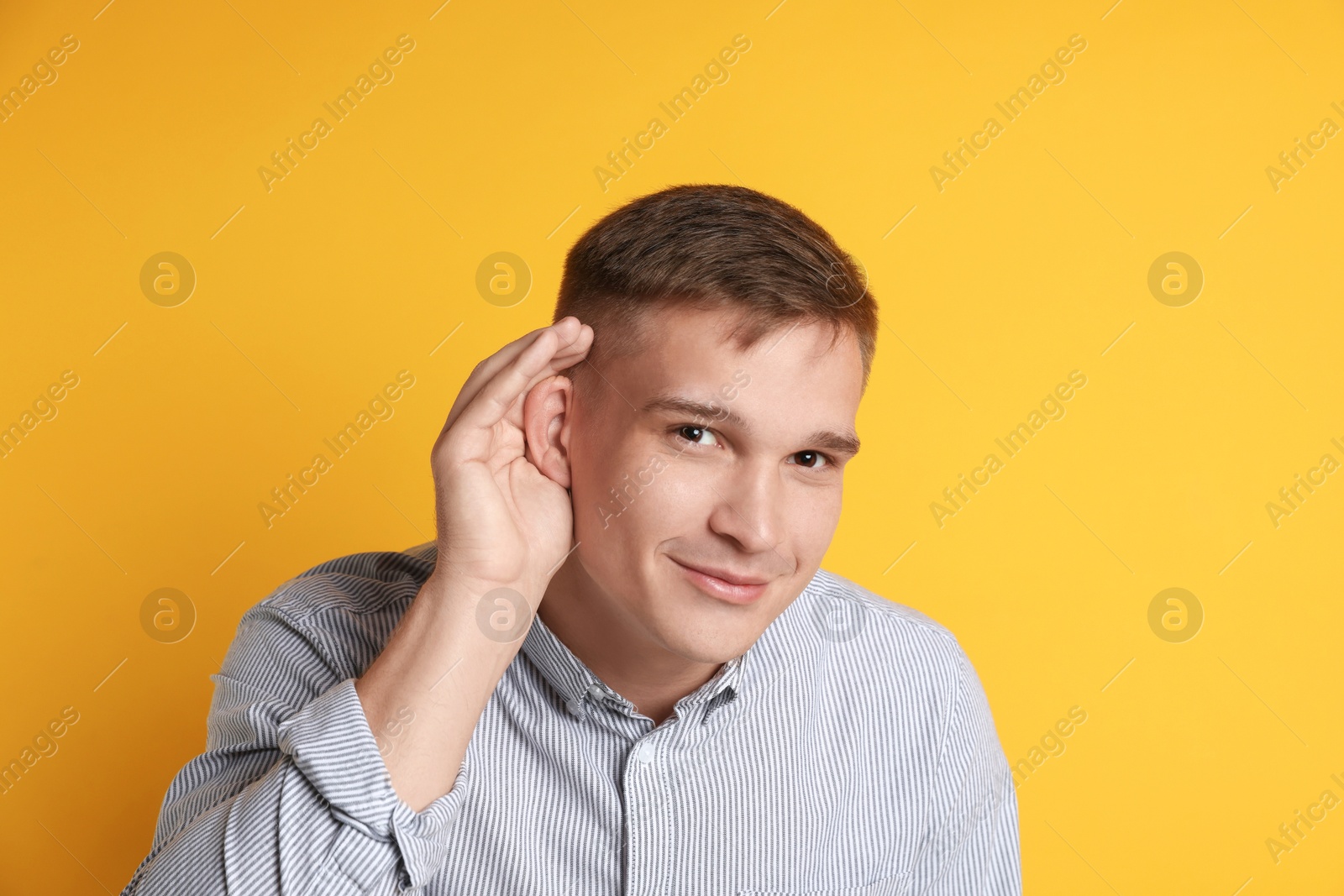 Photo of Man showing hand to ear gesture on orange background