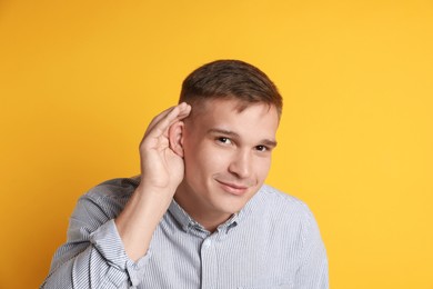 Man showing hand to ear gesture on orange background