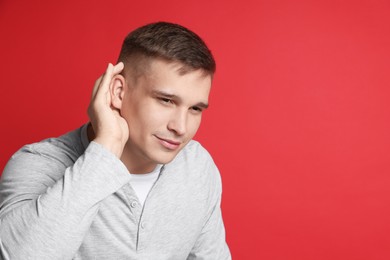 Man showing hand to ear gesture on red background, space for text