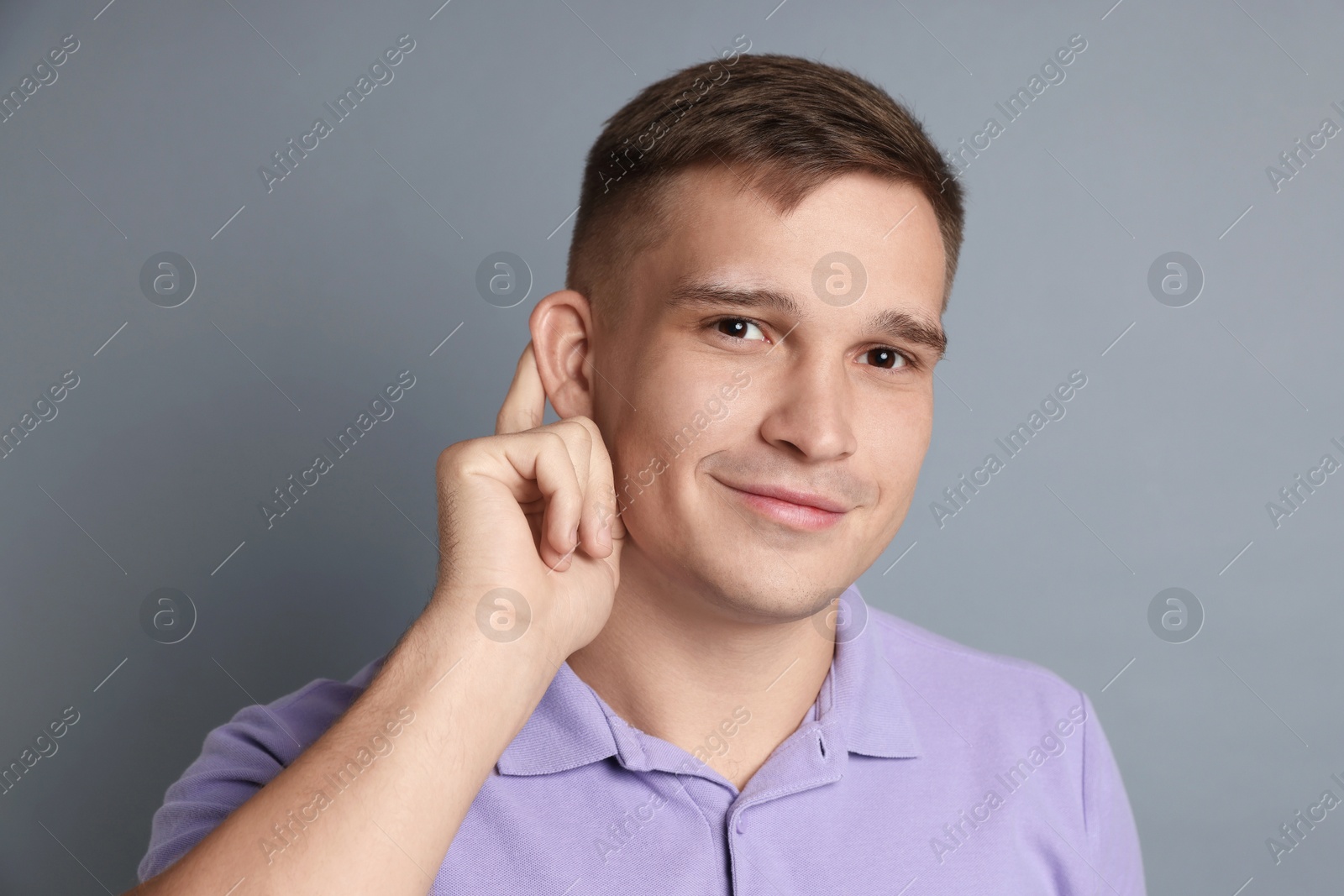 Photo of Man showing hand to ear gesture on gray background