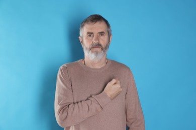 Photo of Mature man making promise on light blue background. Oath gesture