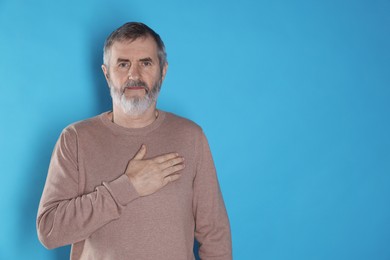 Mature man making promise on light blue background, space for text. Oath gesture