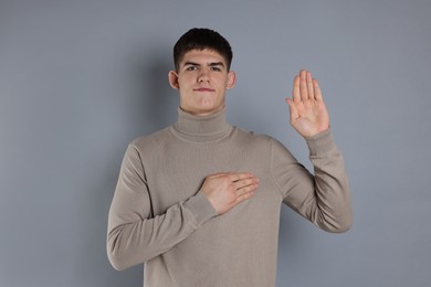 Man showing oath gesture on grey background