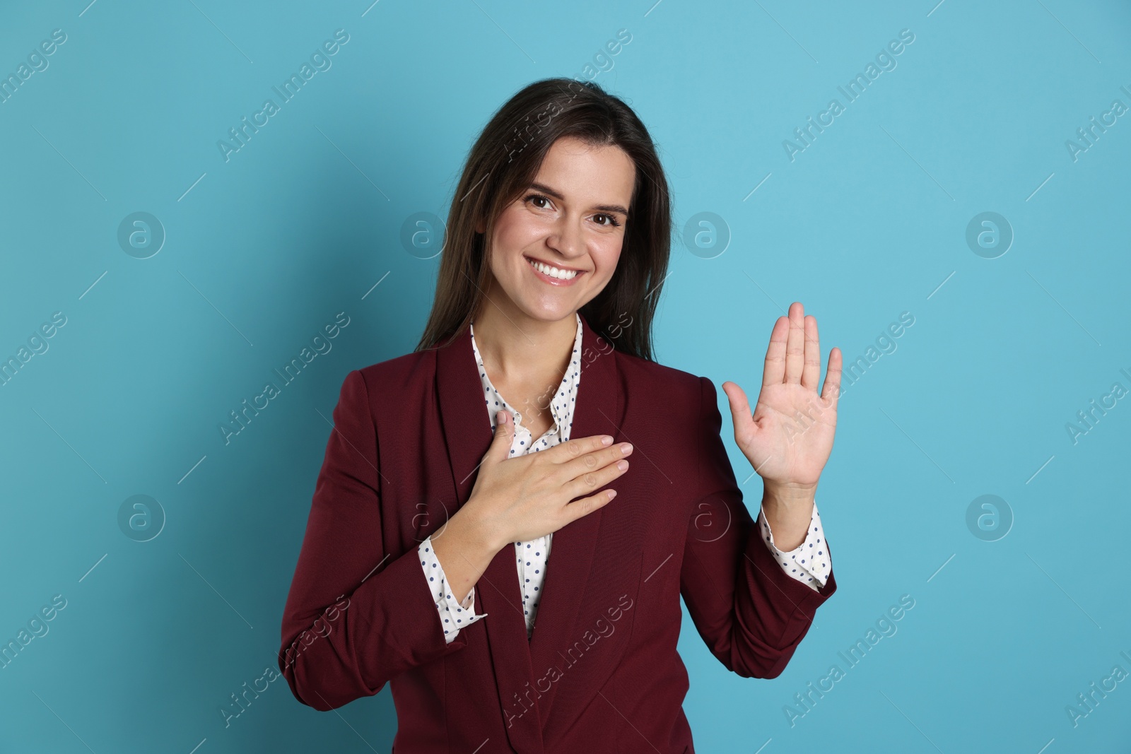 Photo of Woman making promise with raised hand on light blue background. Oath gesture