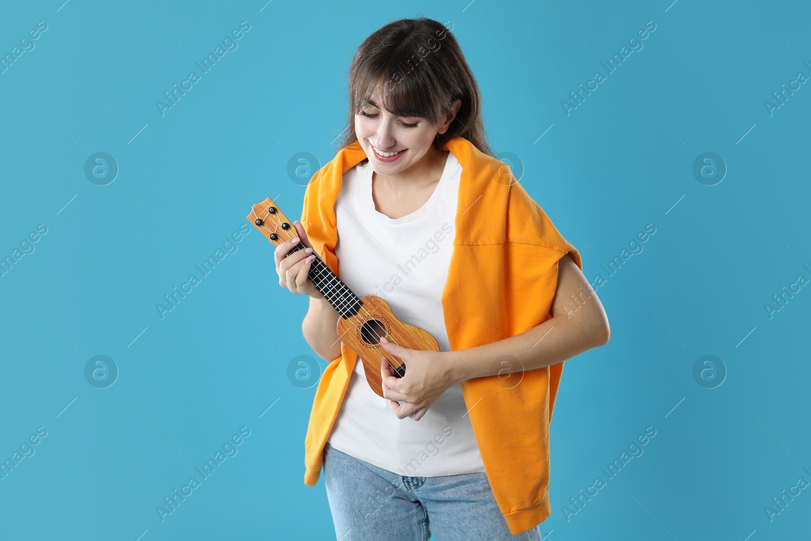 Photo of Happy woman playing ukulele on light blue background