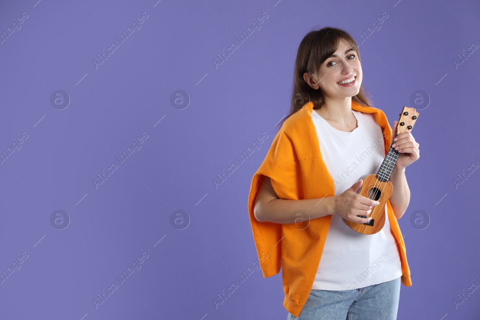 Photo of Happy woman playing ukulele on purple background, space for text