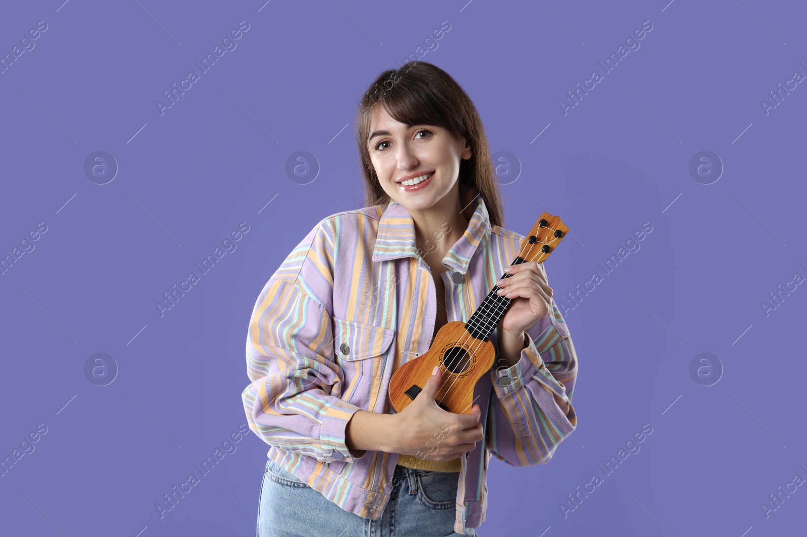 Photo of Happy woman playing ukulele on purple background, space for text