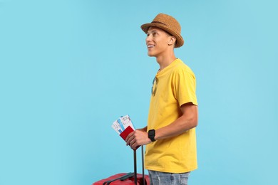 Happy traveller with suitcase, passport and tickets on light blue background. Space for text