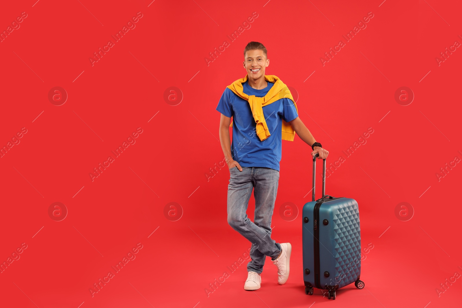 Photo of Happy traveller with suitcase on red background