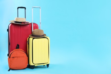 Photo of Travel abroad. Packed suitcases, backpack and hats on light blue background. Space for text