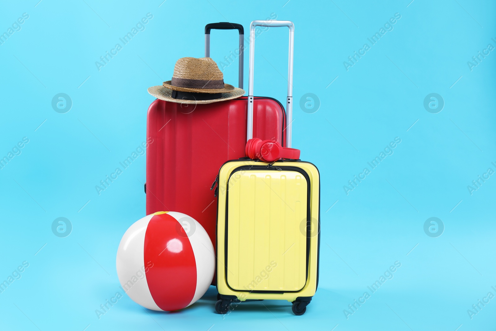 Photo of Travel abroad. Packed suitcases, headphones, hats and beach ball on light blue background