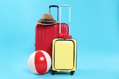 Photo of Travel abroad. Packed suitcases, headphones, hats and beach ball on light blue background