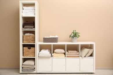 Photo of Folded linens, towels and pillows on shelving unit near beige wall. Home textile storage