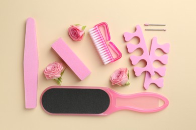 Photo of Set of pedicure tools and flowers on beige background, flat lay