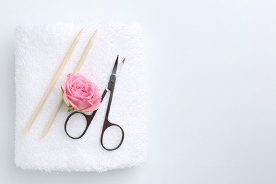 Photo of Pedicure procedure. Towel with scissors, orange sticks and flower on light background, top view. Space for text