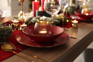 Photo of Christmas place setting with festive decor on wooden table in room, closeup