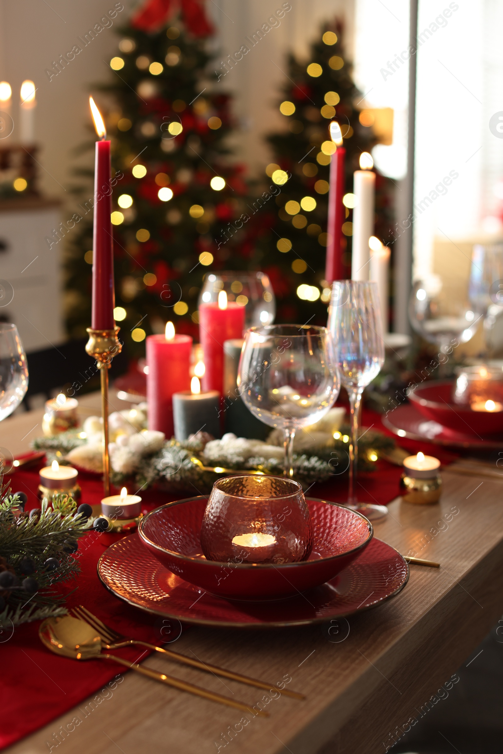 Photo of Christmas table setting with stylish dishware, glasses and burning candles in festive decorated room