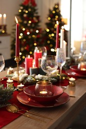 Photo of Christmas table setting with stylish dishware, glasses and burning candles in festive decorated room