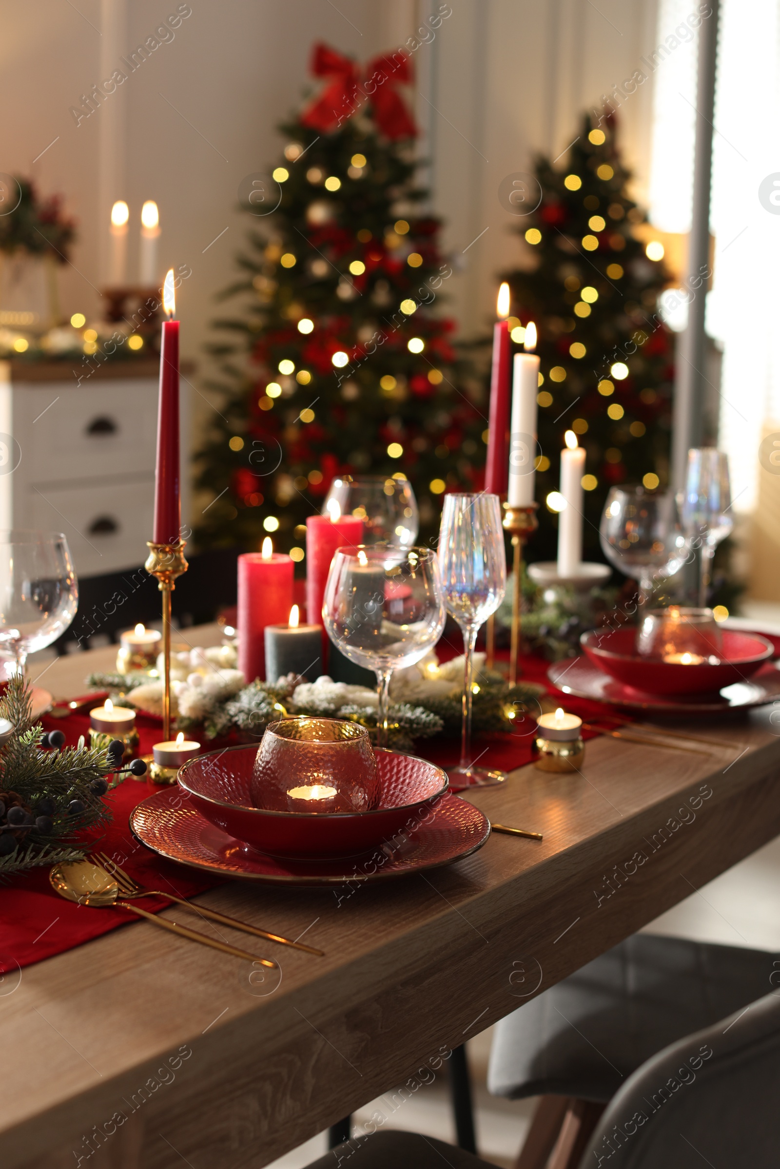 Photo of Christmas table setting with stylish dishware, glasses and burning candles in festive decorated room