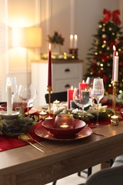 Photo of Christmas table setting with stylish dishware, glasses and burning candles in festive decorated room