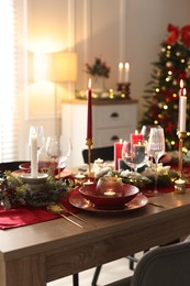 Photo of Christmas table setting with stylish dishware, glasses and burning candles in festive decorated room