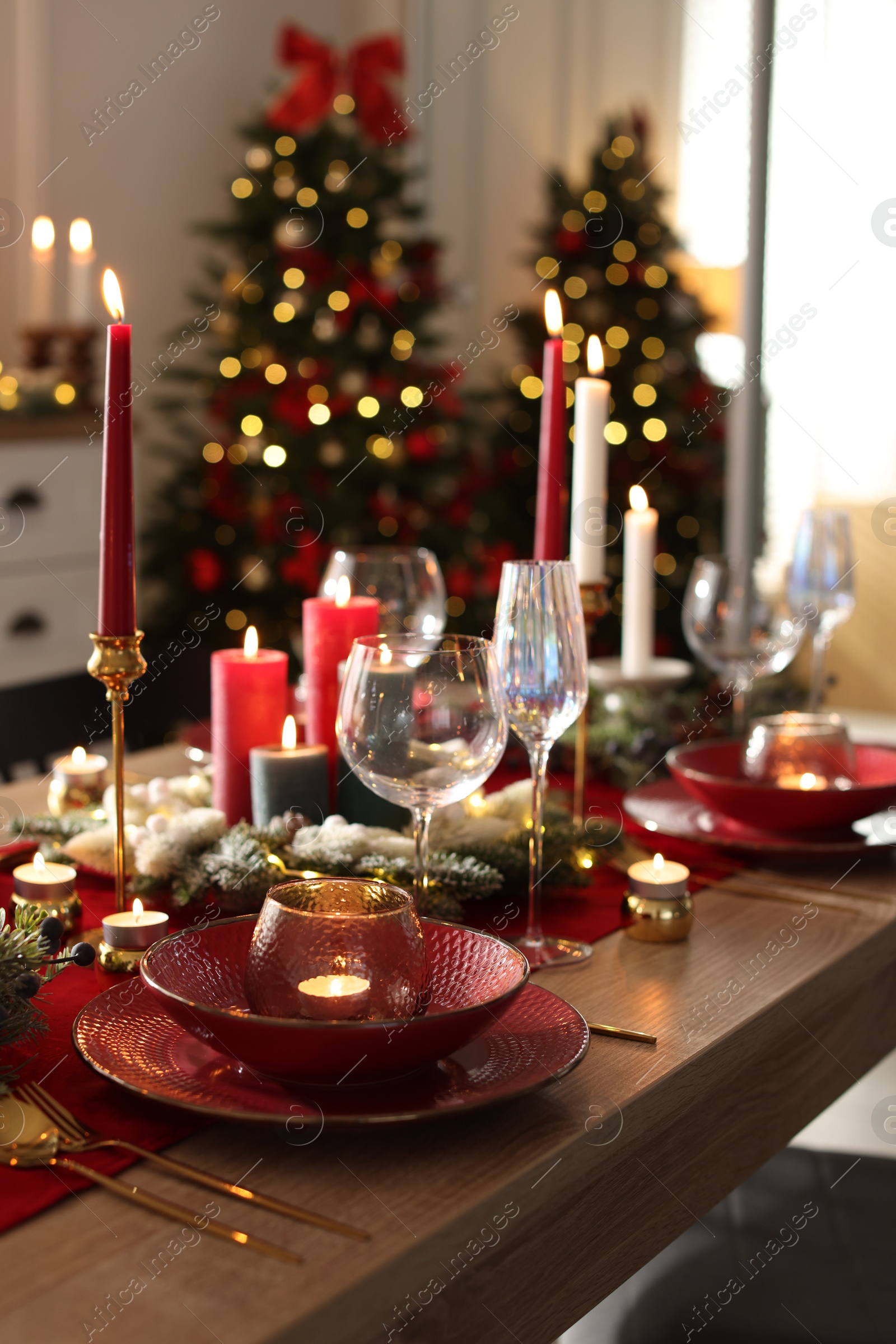 Photo of Christmas table setting with stylish dishware, glasses and burning candles in festive decorated room